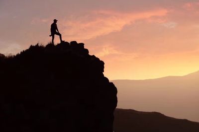 Silhouette of man on rock at sunset