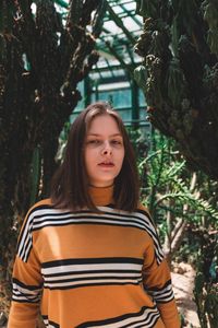 Portrait of beautiful young woman standing against trees