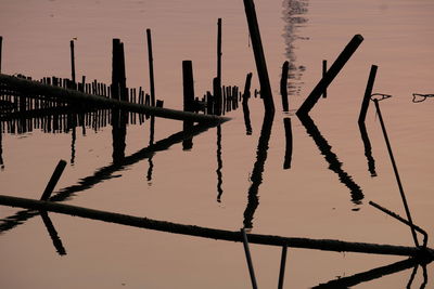 Silhouette wooden posts in lake against sky during sunset