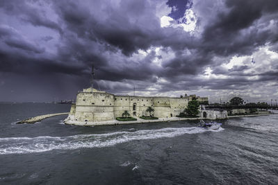 View of building by sea against cloudy sky