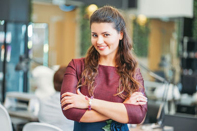 Portrait of smiling young woman standing with arms crossed