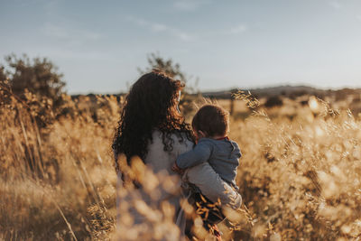 Rear view of mother and daughter by plants against sky