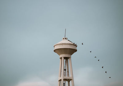 Low angle view of birds flying by tower against sky