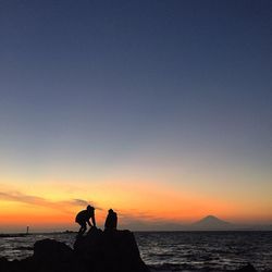 Silhouette couple on rock by beach against sky during sunset