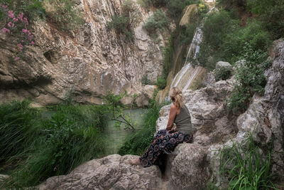 Woman sitting on rock next to a waterfall enjoying nature