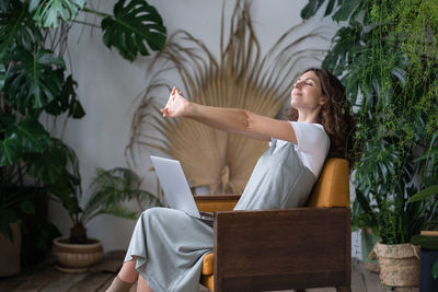 Tired female freelancer stretching arms relaxing while working on laptop in cozy home garden