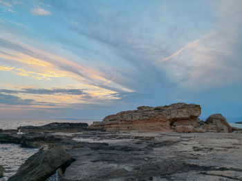 Rock formations on beach against sky during sunset