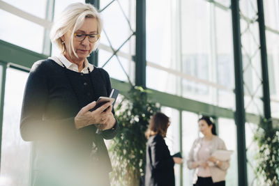 Senior businesswoman using mobile phone while colleagues communicating in background