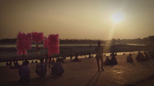 Group of people on shore against sky during sunset