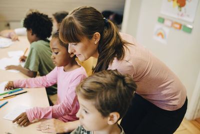 High angle view of teacher guiding students at desk in classroom