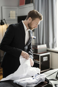 Mature businessman unpacking luggage on bed in hotel room