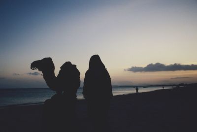 Silhouette couple standing on beach against clear sky during sunset