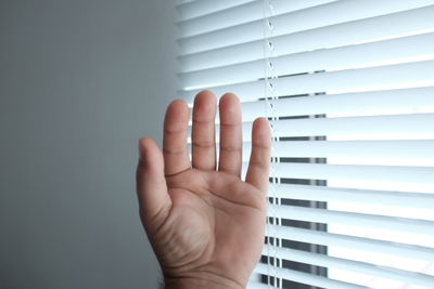 Cropped hand of person by window blinds