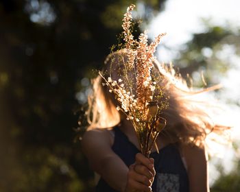 Close-up of woman holding flowering plant against blurred background