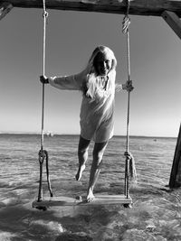 Rear view of boy swinging at beach against sky