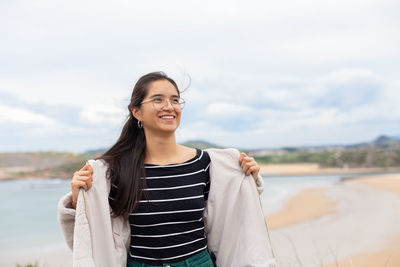 Positive young ethnic female tourist smiling on sandy seashore