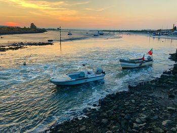 Sailboats moored on sea against sky during sunset