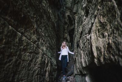 Low angle view of young woman standing amidst rocky mountains