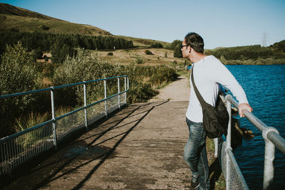 Man standing on bridge over lake against sky