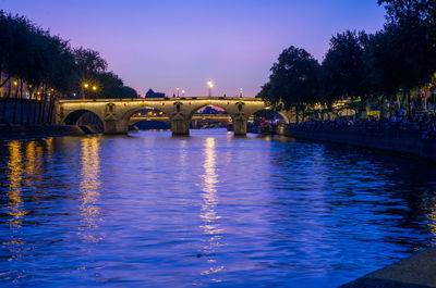 Illuminated bridge over river against sky in city at night