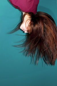 Upside down image of young woman tossing hair against turquoise background