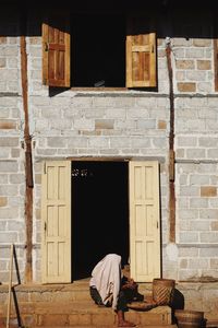 Rear view of man sitting on window of old building