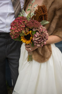 Midsection of bride with bridegroom holding bouquet