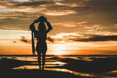 Silhouette woman standing on shore against sky during sunset