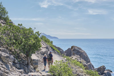 People standing on rock by sea against sky