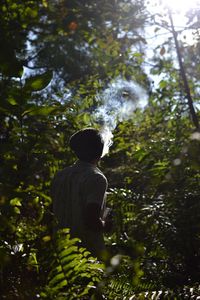 Man exhaling smoke while standing amidst plants