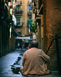 Rear view of man sitting on street amidst buildings