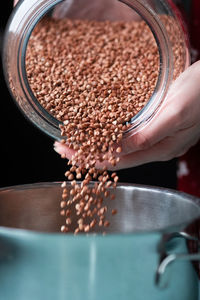 Process how hands of a young woman in a red dress pour buckwheat groats from a large glass jar