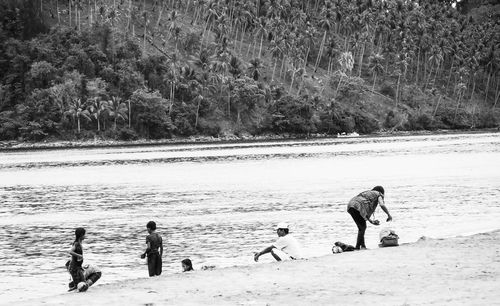 People playing on beach against trees