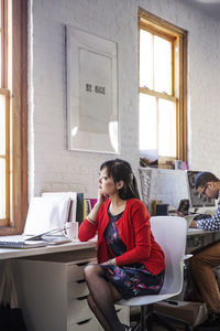 Thoughtful businesswoman looking through window while sitting in office