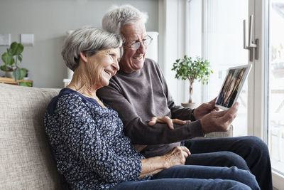 Senior couple sitting in their living room with digital tablet skyping with family