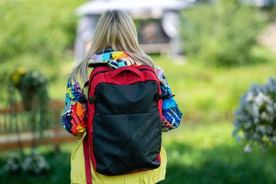 Blonde senior woman in bright clothes with a backpack in the park on a sunny day, rear view