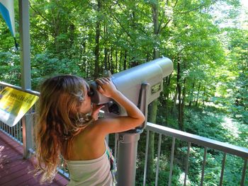 Woman photographing while standing by railing in forest