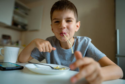 Cheerful, hungry boy eats pasta with appetite, retraction in pasta playfully