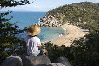 Rear view of woman sitting on rock by sea