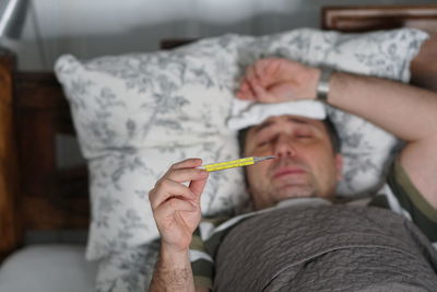 Man checking temperature while lying on bed at home