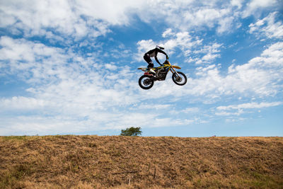 Low angle view of man jumping motorcycle over field against cloudy sky