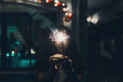 Teenage girl holding sparkler at night