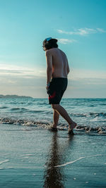 Shirtless man standing at beach against sky