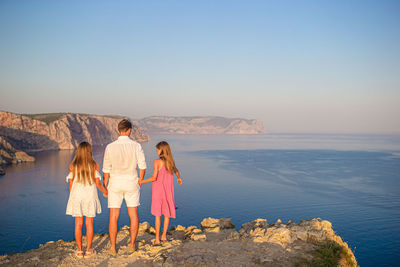 Rear view of women standing on rock by sea against sky