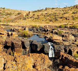 Rocks on field by river against sky