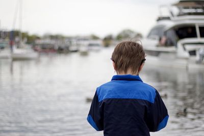 Rear view of boy standing on boat against sky
