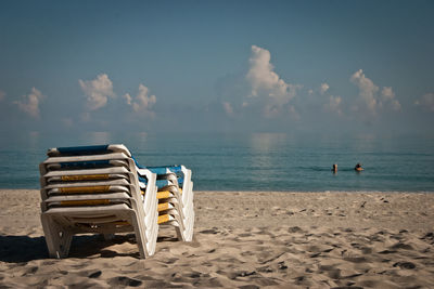 Deck chairs on beach against sky