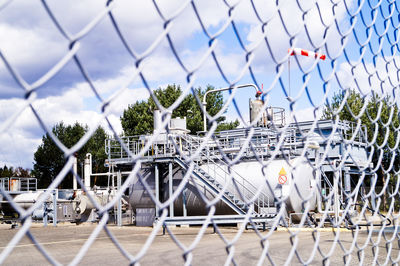 Equipment against cloudy sky seen through chainlink fence