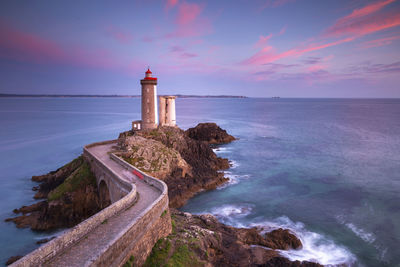 Lighthouse by sea against sky during sunset