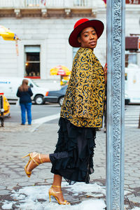 Portrait of woman leaning on pole while standing at footpath in city